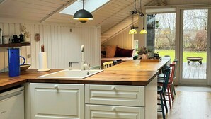 Eine moderne Küche mit einer Holzinsel, weißen Schränken und einem großen Fenster mit Blick auf einen Garten.