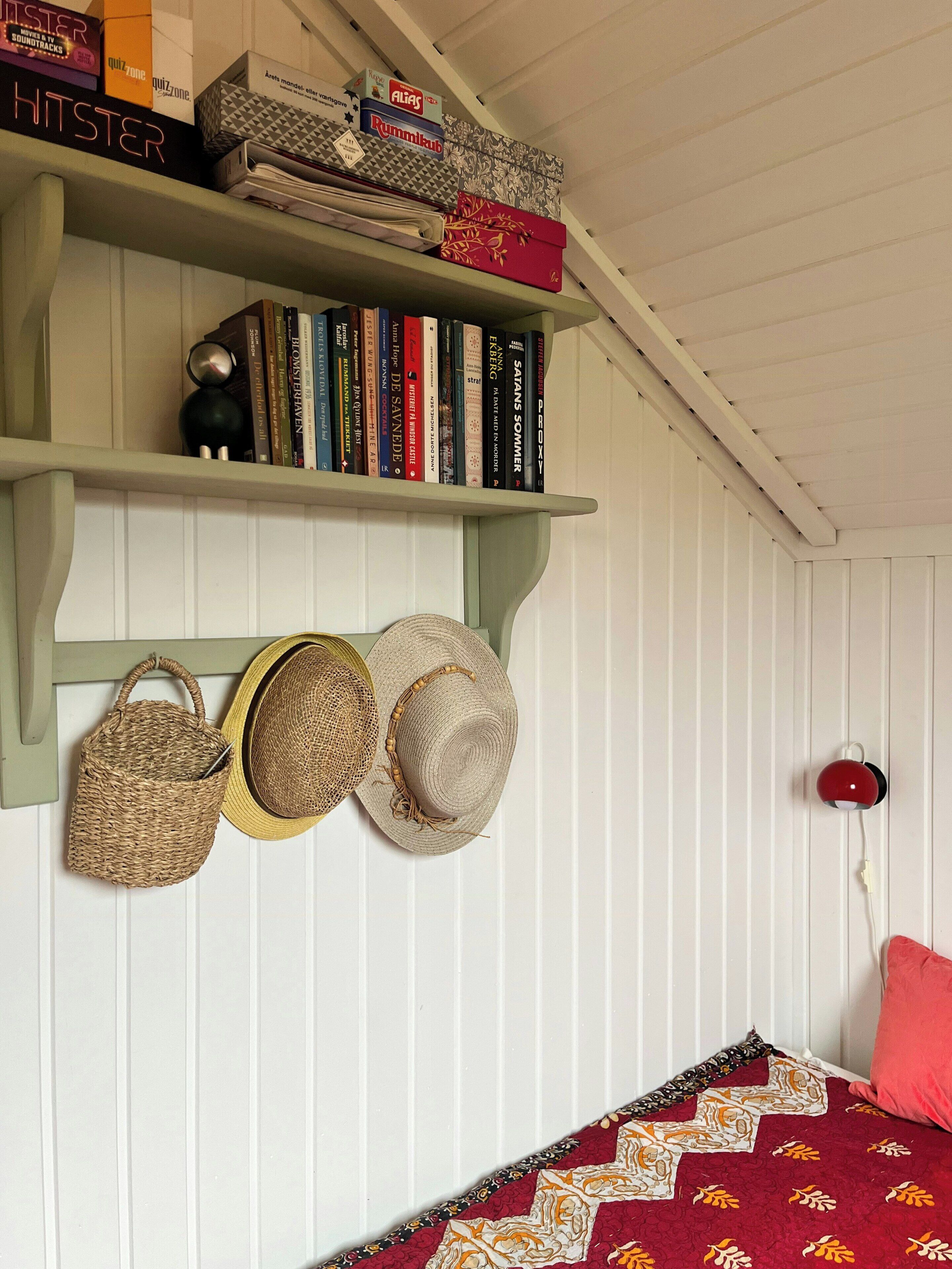 Um quarto com uma estante de livros, uma cama com colcha estampada e um porta-chapéus fixado na parede.