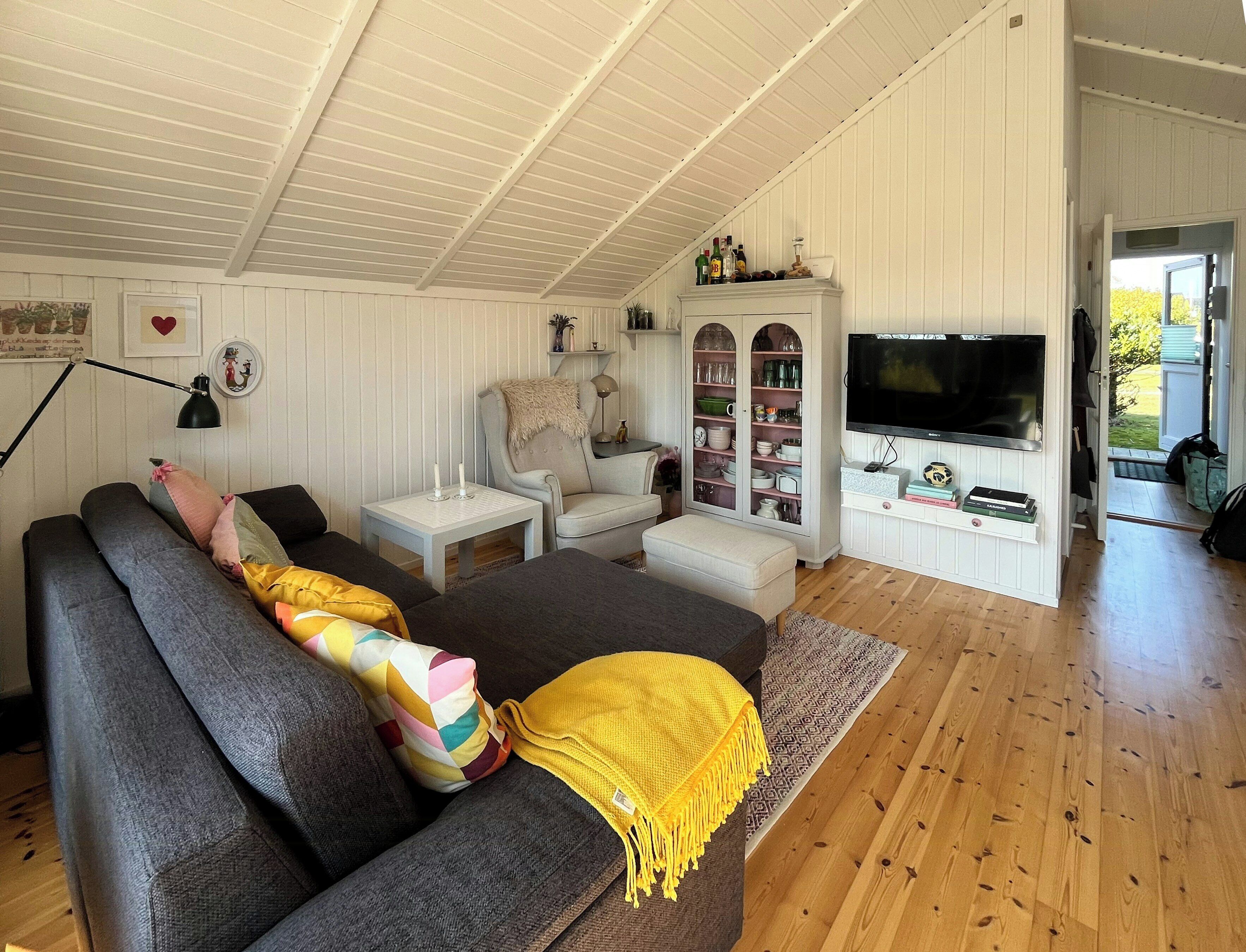 Un salon confortable avec un canapé, un téléviseur, un meuble avec des portes en verre et un plancher en bois.