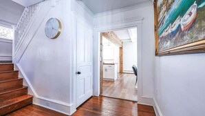 A staircase leading to a room with a clock, a painting, and a view into another room with wooden floors.