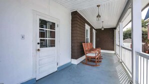 A covered porch with a white door, a brick wall, and two rocking chairs.