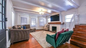 A living room with a fireplace, wooden floors, a sofa, and a staircase.