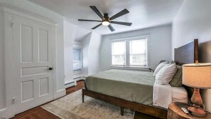 A bedroom with a bed, a ceiling fan, a window, a nightstand, and a lamp.