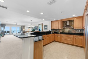A spacious kitchen with wooden cabinets, a black countertop, and a view to the outside.