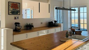 Una cocina moderna con encimera de madera, armarios blancos, iluminación colgante y un amplio ventanal con vistas.