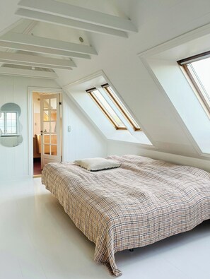 A bedroom with a sloped ceiling, skylights, a bed with a patterned bedspread, and a door leading to another room. - Villa with fjord view by Frederik VII's Canal (Løgstør)