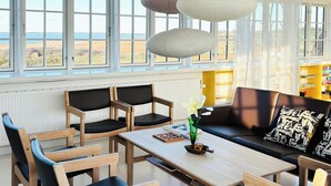 Una sala de estar moderna con sofá, sillas, una mesa y ventanas grandes con vistas.