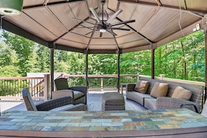 A covered outdoor seating area with wicker furniture, a ceiling fan, and a view of a wooded area. - Forest Cove · Cozy, Secluded w/ Hot Tub & More (Mineral)