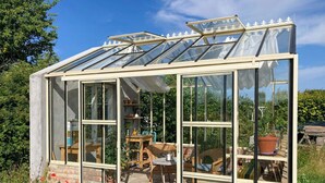 A glass greenhouse with a brick exterior, wooden furniture inside, and a clear view of the surrounding garden. - Holiday home with greenhouse near Mälarhusen (Skåne län)
