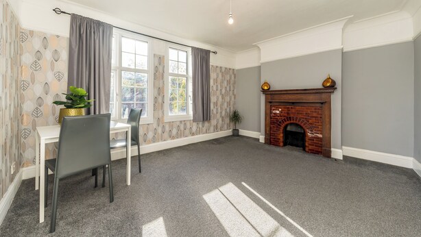 A room with a dining table, chairs, a fireplace, and a window with curtains. - Two bed High Street Apartment (Teddington)