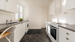 A kitchen with white cabinets, a washing machine, a stove, and a sink. - Two bed High Street Apartment (Teddington)