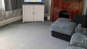 A living room with a television on a cabinet, a fireplace, and a sofa. - Two bed High Street Apartment (Teddington)