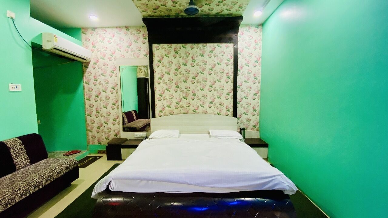 A bedroom with a bed, a sofa, a mirror, and an air conditioning unit.