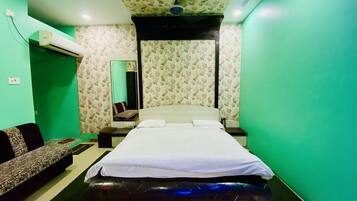 A bedroom with a bed, a sofa, a mirror, and an air conditioning unit.