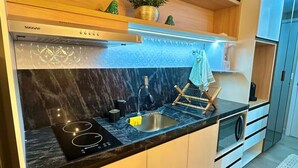 A modern kitchen with a built-in stove, a sink, wooden cabinets, and a decorative plant. - Jampa House - Your beachfront apartment in Bessa (João Pessoa)