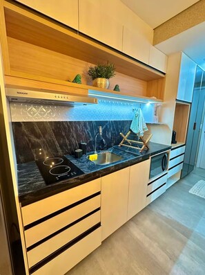 A modern kitchen with a built-in stove, a sink, wooden cabinets, and a decorative plant. - Jampa House - Your beachfront apartment in Bessa (João Pessoa)