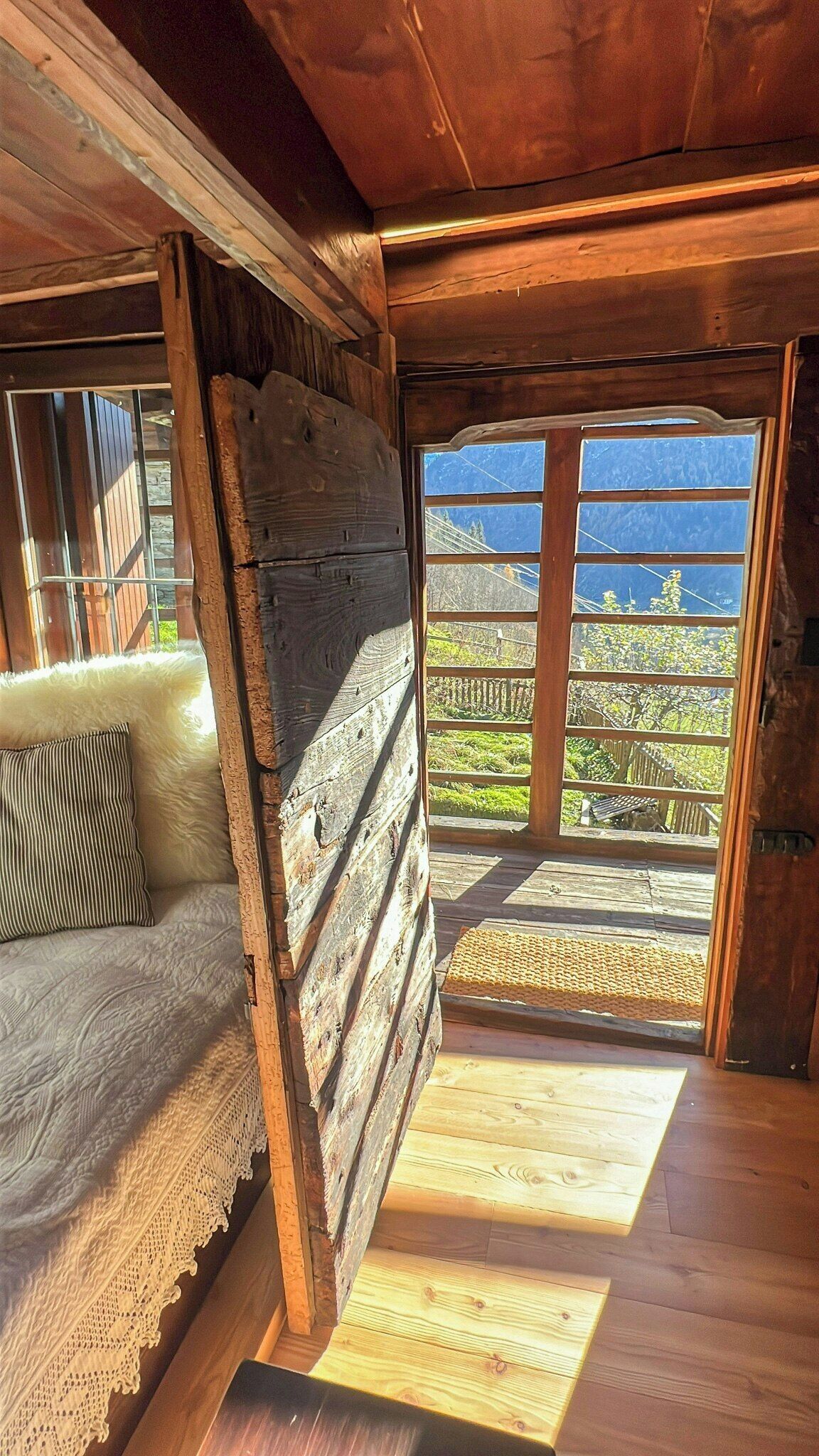 A wooden interior with a sofa, a view through a window, and a wooden floor.