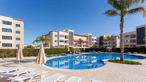 A swimming pool with lounge chairs, a palm tree, and modern buildings in the background. - Sea Breeze Lagos, Modern Apartment with Pool and Garden View – Lagos (Lagos)