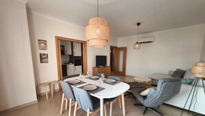 A modern living room with a dining area, a sofa, and a TV. - Sea Breeze Lagos, Modern Apartment with Pool and Garden View – Lagos (Lagos)