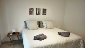 A bed with striped bedding, pillows, and rolled towels. There is a small table with a lamp and a phone. Three artworks are displayed on the wall above the bed. - Sea Breeze Lagos, Modern Apartment with Pool and Garden View – Lagos (Lagos)