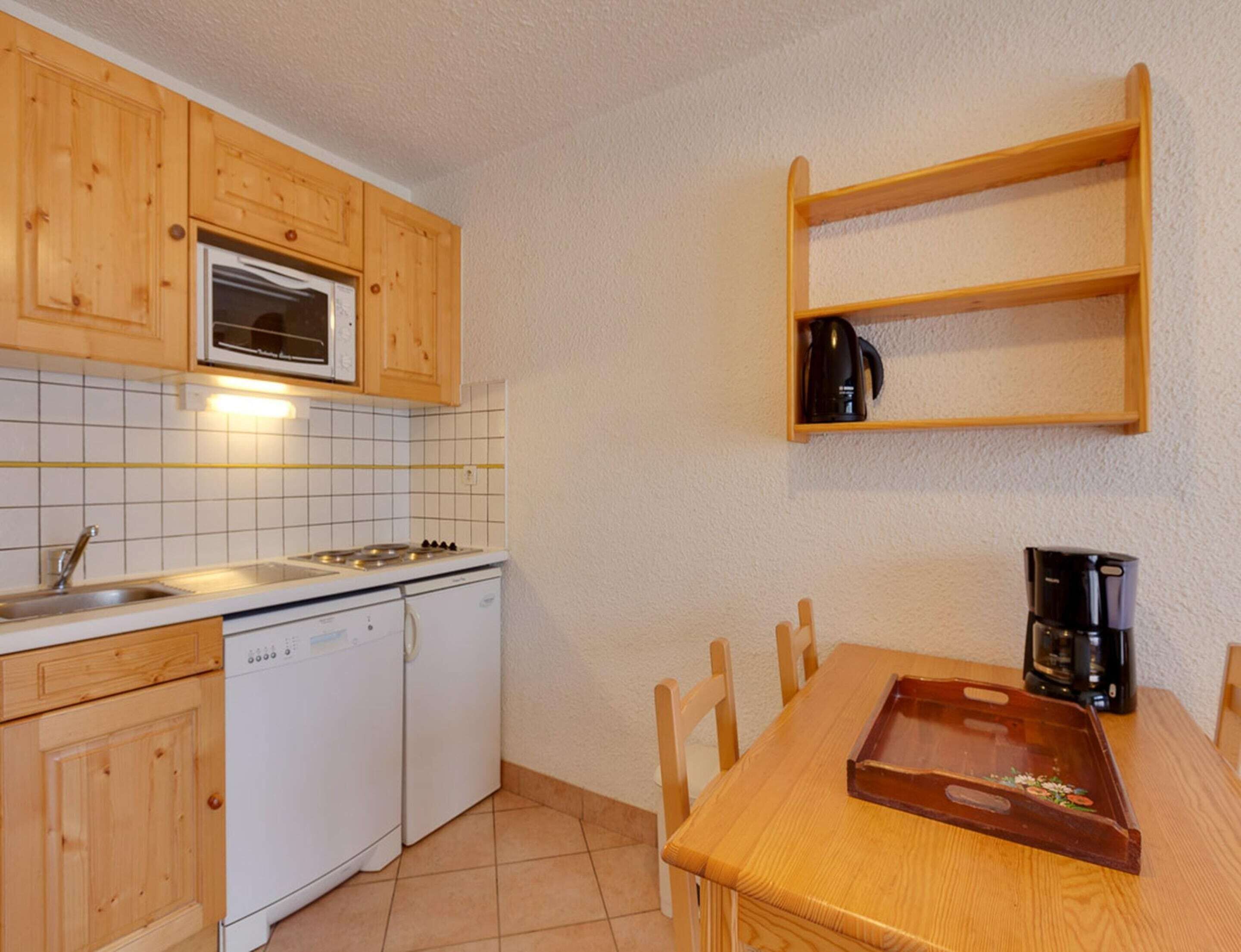 A compact kitchen with wooden cabinets, a microwave, a stove, a dishwasher, a coffee maker, and a wooden table with chairs.