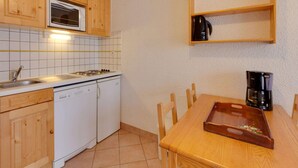 Una cocina compacta con armarios de madera, microondas, estufa, lavavajillas, cafetera y una mesa de madera con sillas.