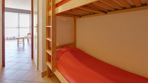 Una cama litera con colchón rojo, cabecero de madera y ventana con vista a un balcón.