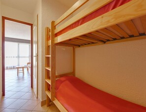 Ein Etagenbett mit roter Matratze, einem Holzkopfstück und einem Fenster mit Blick auf einen Balkon.