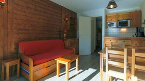 Una sala de estar acogedora con un sofá de madera, una mesita pequeña de madera y una zona de cocina con armarios y electrodomésticos de madera.