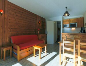 Ein gemütliches Wohnzimmer mit einer Holzsofa, einem kleinen Holztisch und einer Küchenzeile mit Holzschränken und Geräten.