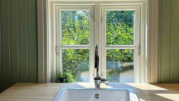 A bathroom with a white sink, two windows, and a view of greenery outside.
