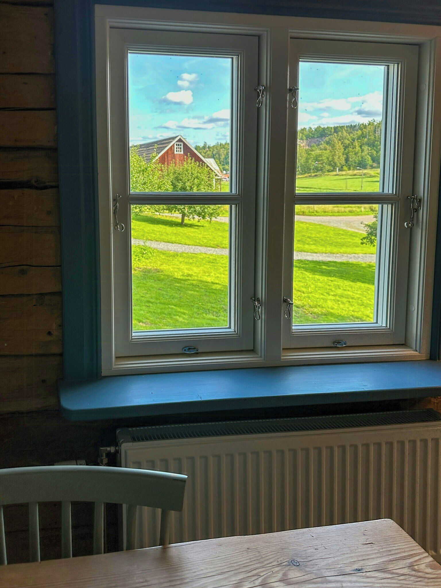 A room with a large window overlooking a green landscape, a radiator below, and a wooden table in the foreground.