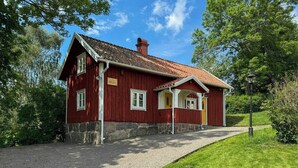 A red wooden house with a stone foundation, a gravel driveway, and a well-maintained lawn.