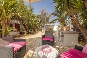 Eine Terrasse im Freien mit Korbmöbeln, einer weißen Tischdecke und einem roten Kissen.