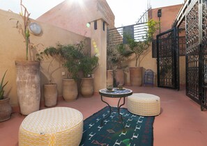 A courtyard with large potted plants, a round table, and a patterned rug. - Riad elkhamsa maison Privé avec petite déjeuner inclus (Marrakech)