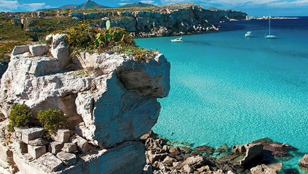 Eine Küstenlandschaft mit klarem türkisblauem Wasser, felsigen Klippen und mehreren Segelbooten.