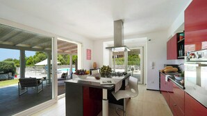 Eine moderne Küche mit einer zentralen Kochinsel, einem Essbereich mit einer Bank und Blick auf einen Pool und Grünflächen.