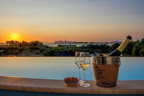 Blick auf einen Pool bei Sonnenuntergang, mit einer Champagnerflasche und Gläsern.