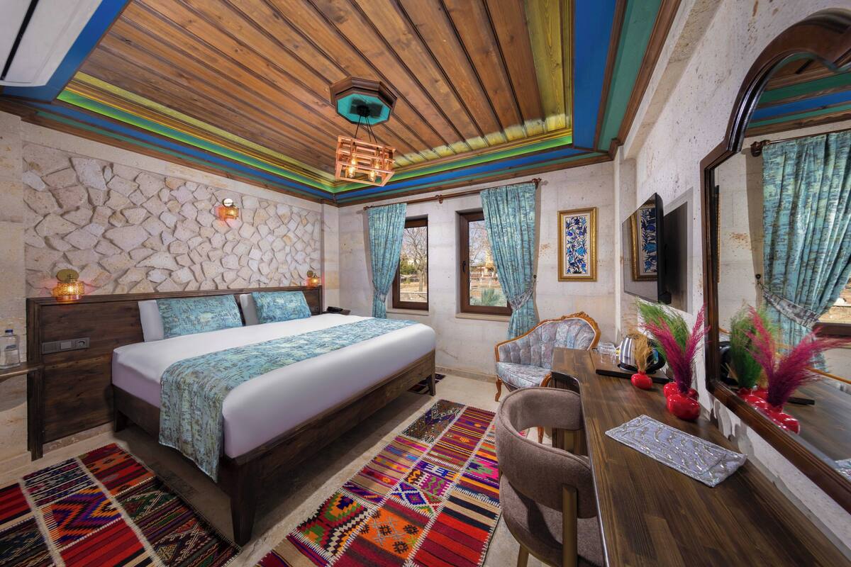 A bedroom with a bed, a desk, a chair, a mirror, and a stone wall.
