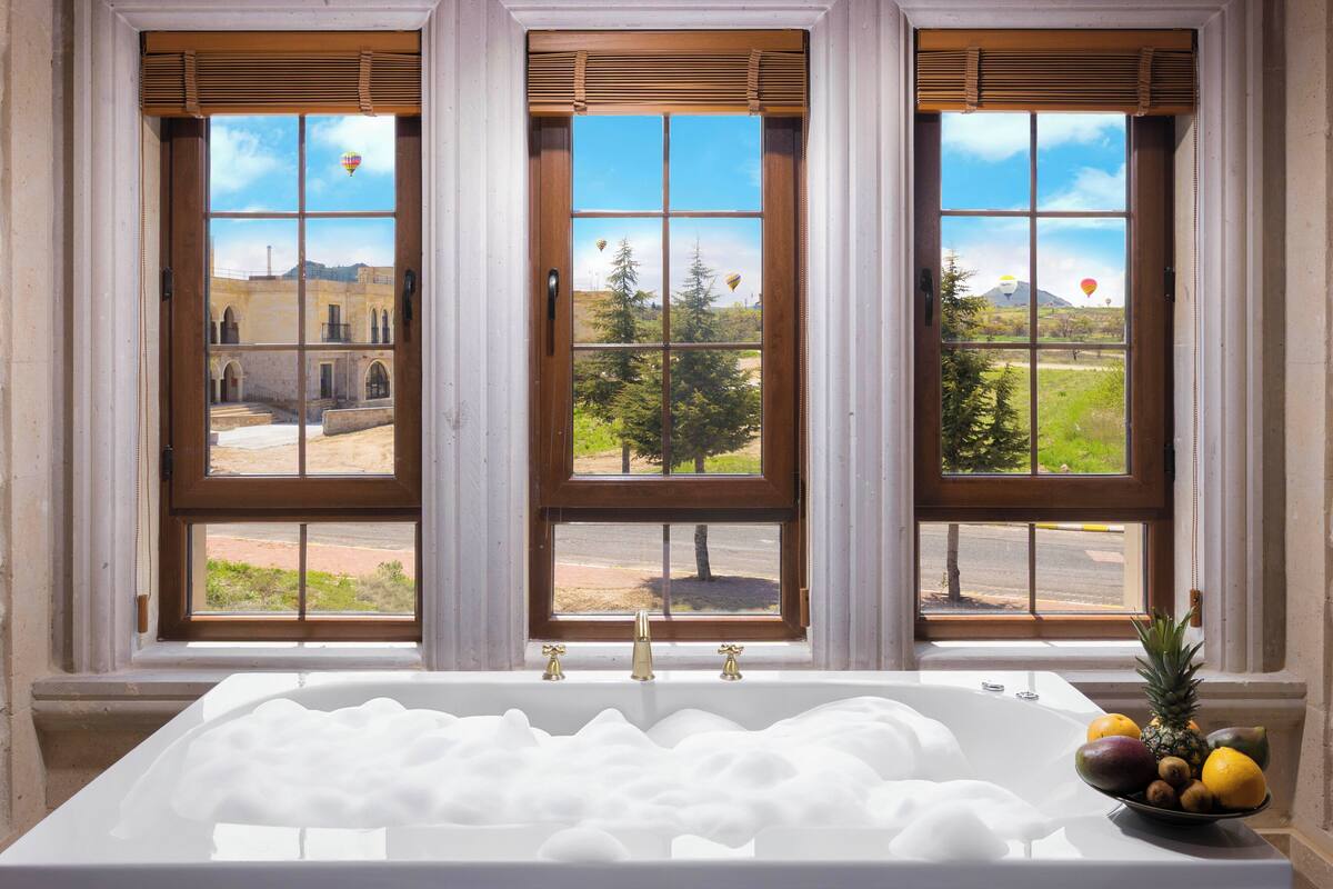 A bathroom with a bathtub, a window with three panes, and a bowl of fruit on the windowsill.