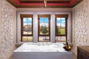 A bathroom with a large bathtub, stone walls, and three windows with wooden frames. - Cappadocia Golden Elite (Nevsehir)