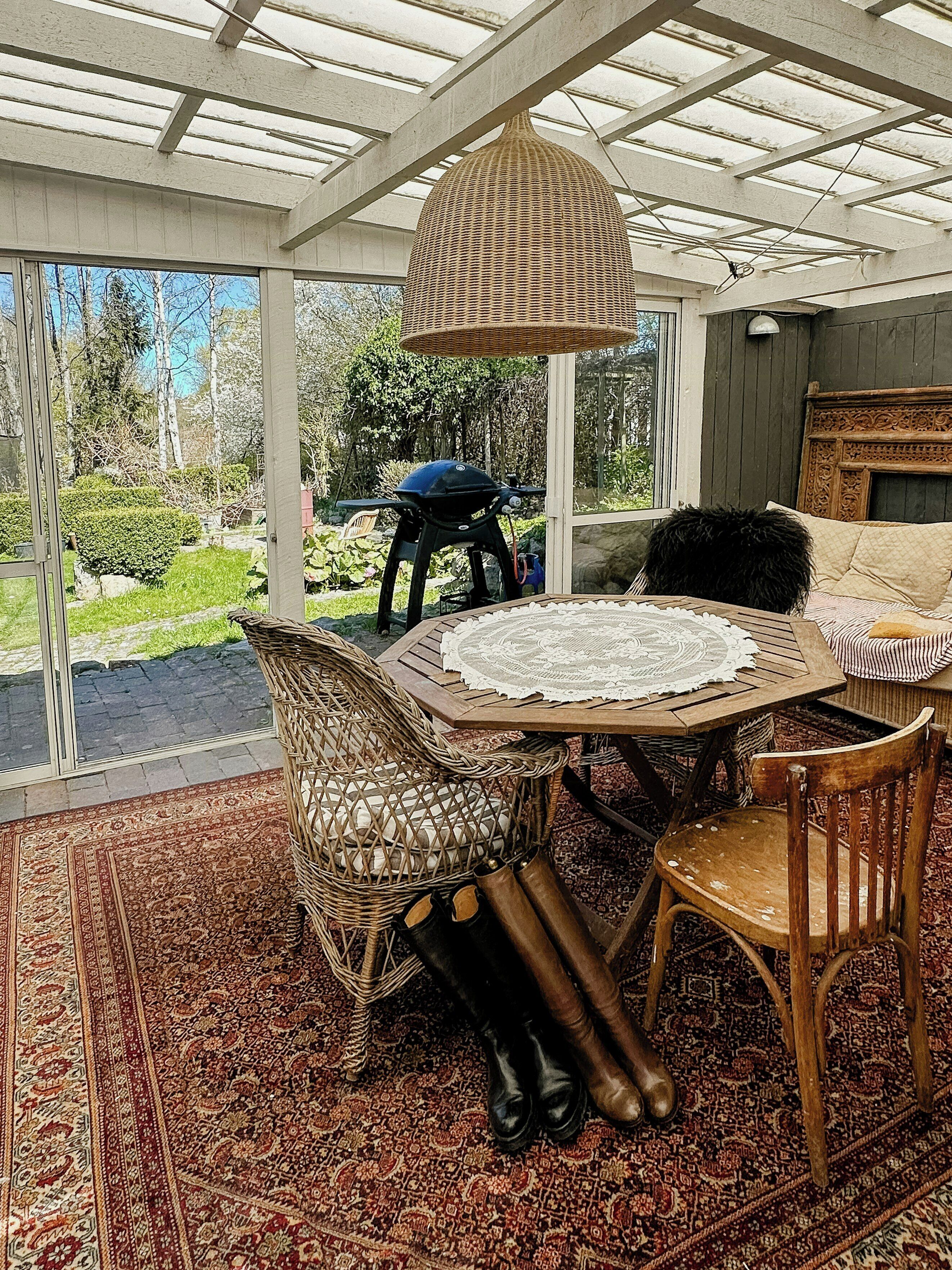 A conservatory with wicker furniture, a table with a lace tablecloth, and a view of the garden.