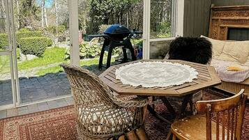 A conservatory with wicker furniture, a table with a lace tablecloth, and a view of the garden.