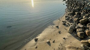 En strand med en stenig kust och stilla vatten som speglar solen.