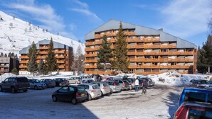 Ett hotell med flera våningar och balkonger, en parkeringsplats full av bilar och ett snöklätt berg i bakgrunden.