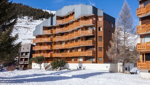 Ett hotell med flera våningar och balkonger, en skidbacke i bakgrunden och ett snötäckt område.