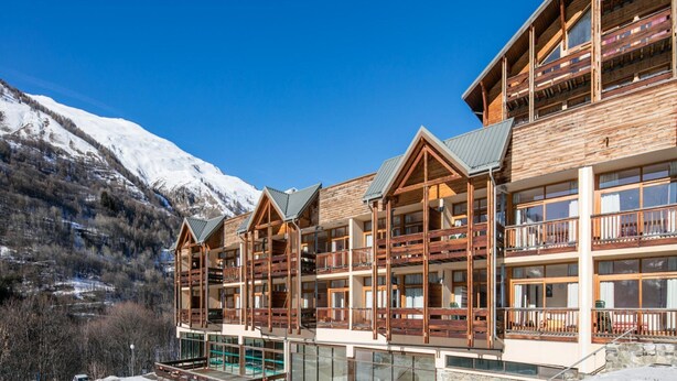 Un hotel a più piani con balconi, ampie finestre e vista sulle montagne innevate.