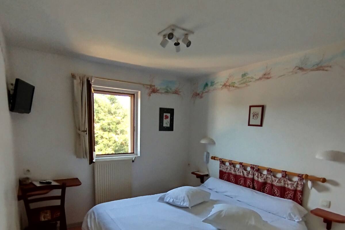 Un dormitorio con una cama, un escritorio, una silla, un ventanal y un radiador.