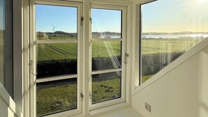 A room with a large window, a cushioned bench, and a view of a green landscape.