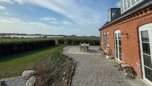 A brick building with a gravel driveway, a patio with outdoor seating, and a view of the countryside.